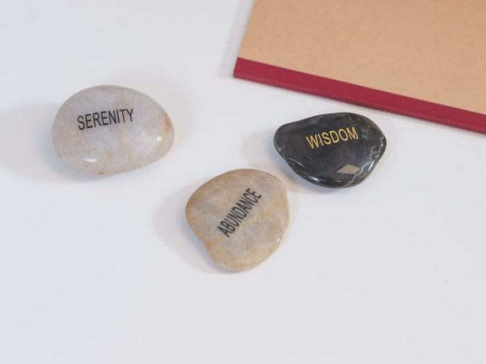 Three polished, semiprecious stones engraved with the words serenity, abundance, and wisdom.