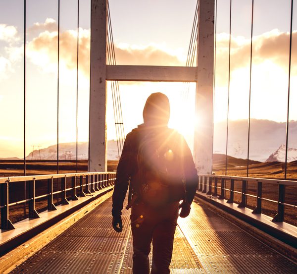Man walking on bridge towards mountains and sunset