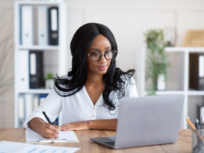 Happy black young business woman looking at computer