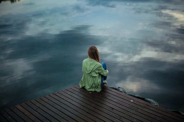 woman sitting on dock looking out at dark water