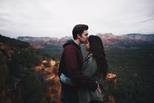 man kissing his girlfiend on forehead with mountain overlook behind them