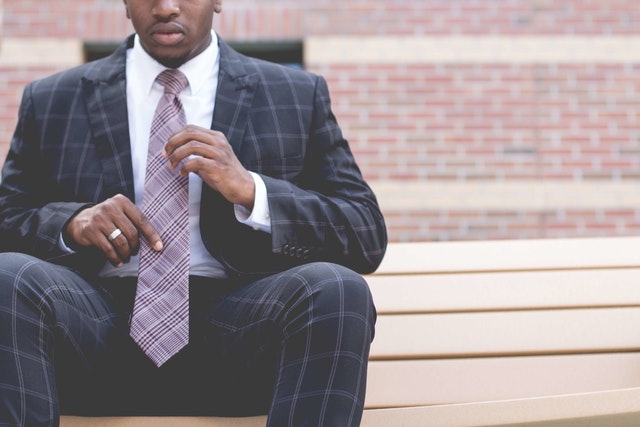 man of color in suit sitting on bench adjusting his tie