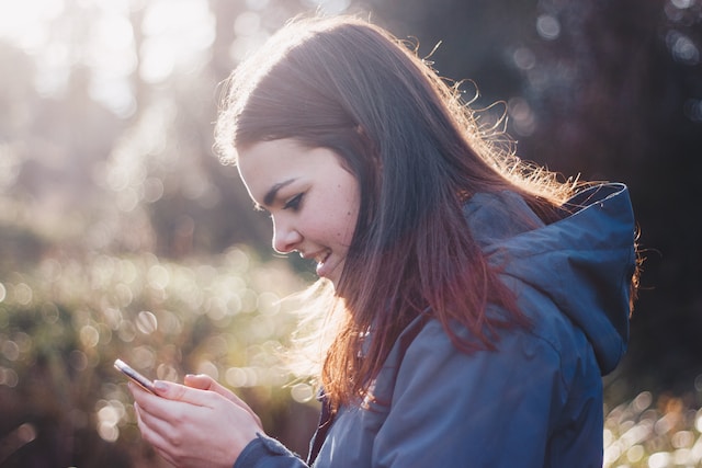 photo of an older teen girl standing looking down at her phone smiling