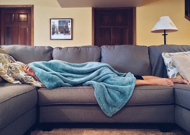 photo of a person laying on a couch underneath a blanket with only their feet showing